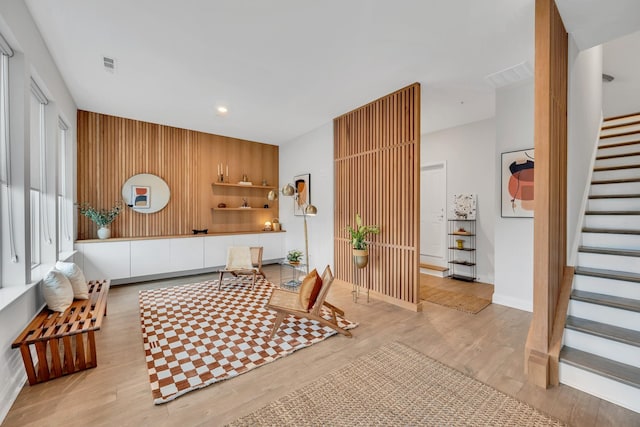 living area with stairs, light wood-type flooring, visible vents, and baseboards