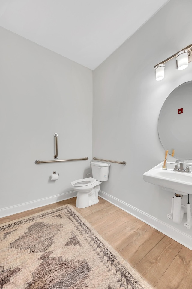 half bathroom with toilet, a sink, baseboards, and wood finished floors