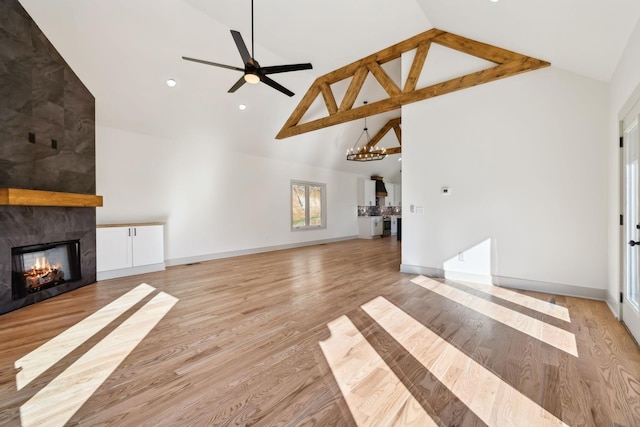 unfurnished living room featuring a fireplace, high vaulted ceiling, light wood-type flooring, baseboards, and ceiling fan with notable chandelier