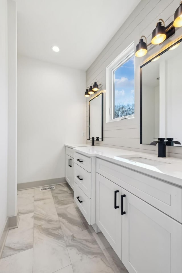 bathroom featuring marble finish floor, a sink, wooden walls, and double vanity