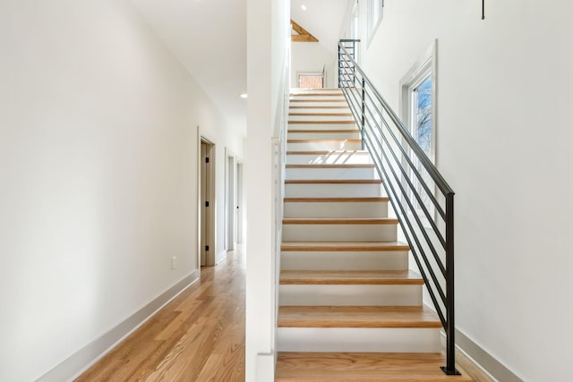 staircase featuring a high ceiling, baseboards, and wood finished floors