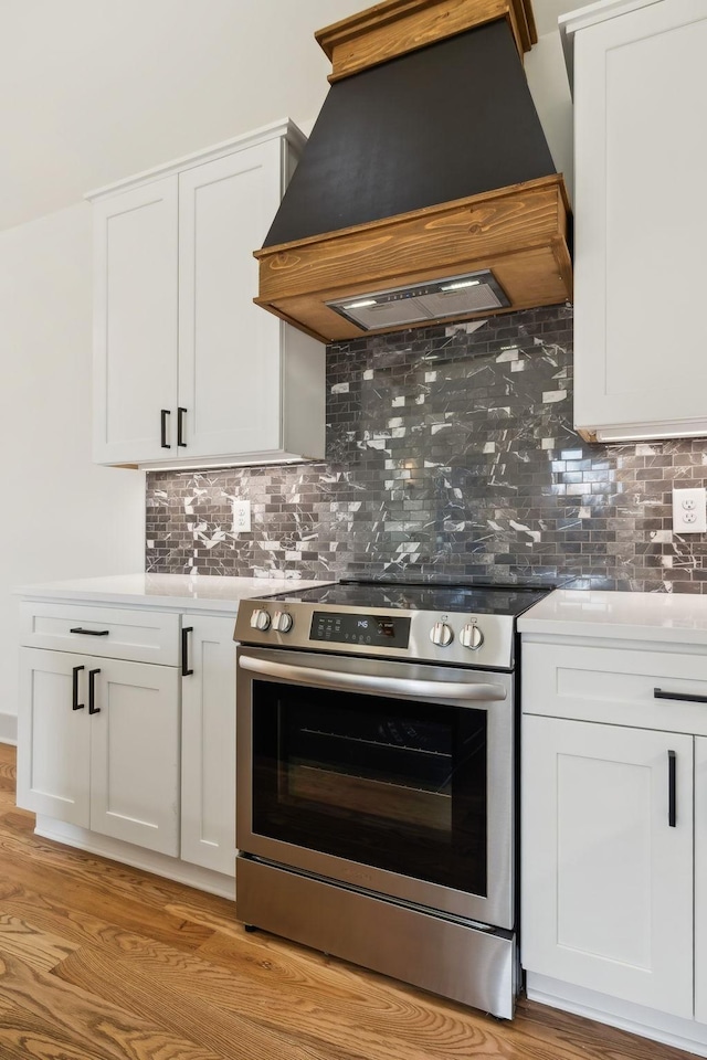 kitchen featuring premium range hood, light wood-style floors, white cabinets, stainless steel electric stove, and tasteful backsplash