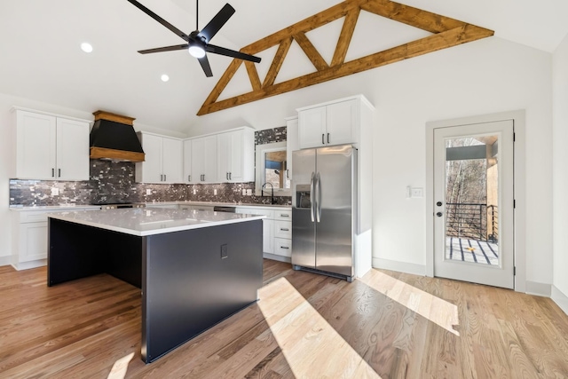 kitchen with a sink, stainless steel refrigerator with ice dispenser, a center island, light wood finished floors, and custom range hood