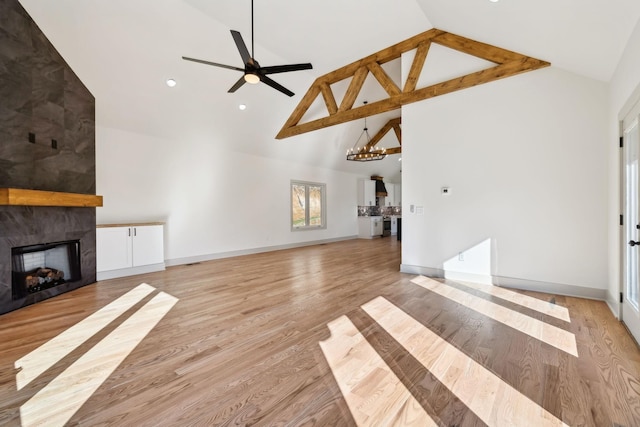 unfurnished living room with high vaulted ceiling, a large fireplace, ceiling fan with notable chandelier, baseboards, and light wood finished floors