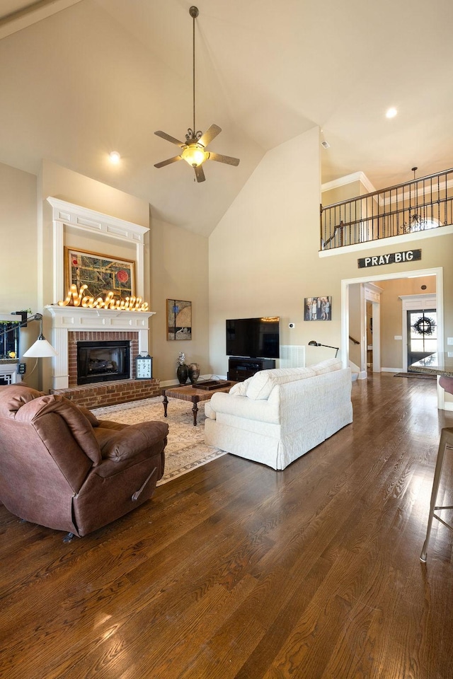 living area featuring ceiling fan, high vaulted ceiling, a brick fireplace, and wood finished floors