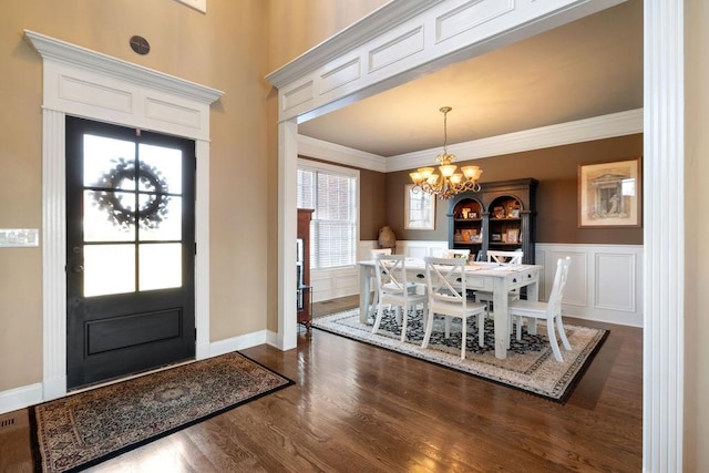 entrance foyer featuring dark wood finished floors, crown molding, a decorative wall, an inviting chandelier, and wainscoting