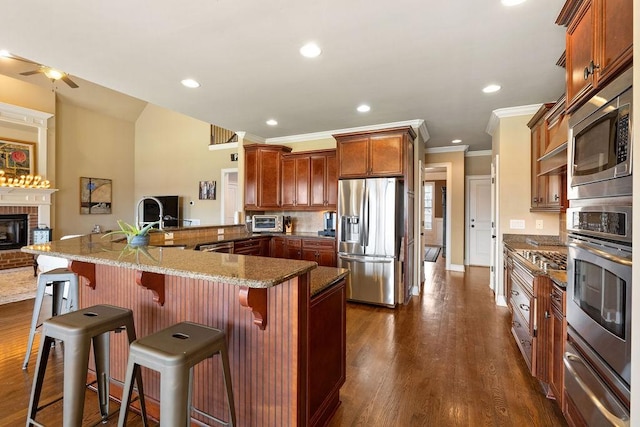 kitchen with dark wood-style flooring, a warming drawer, appliances with stainless steel finishes, a brick fireplace, and dark stone countertops