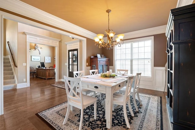 dining space featuring wainscoting, dark wood-style flooring, an inviting chandelier, stairs, and crown molding