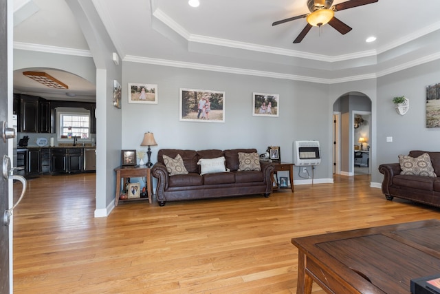 living area with heating unit, light wood finished floors, arched walkways, and a raised ceiling