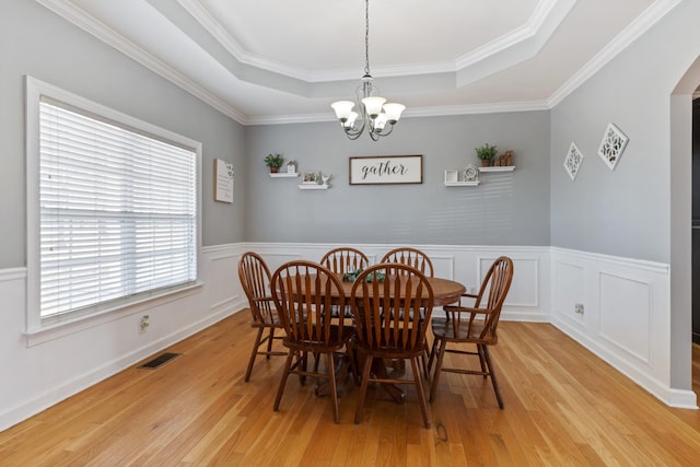 dining area featuring visible vents, a raised ceiling, a wainscoted wall, light wood-type flooring, and a notable chandelier