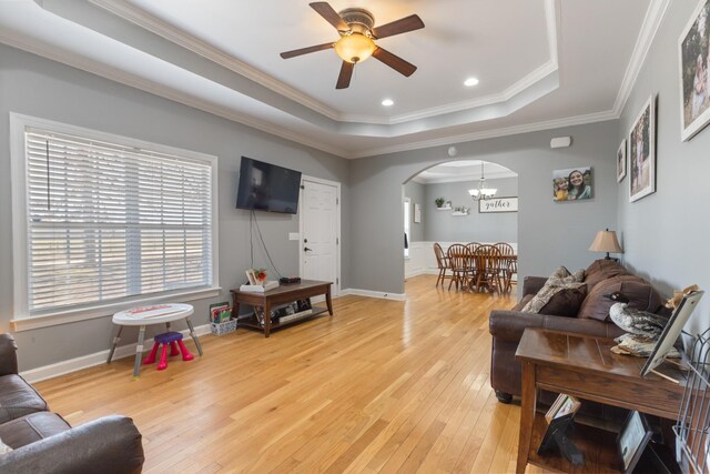 living room with light wood finished floors, baseboards, arched walkways, a raised ceiling, and crown molding