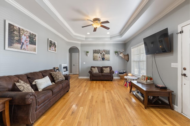 living area featuring arched walkways, light wood-style floors, heating unit, a raised ceiling, and crown molding