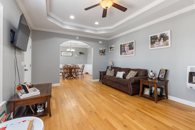 living area featuring arched walkways, ornamental molding, light wood-type flooring, heating unit, and a tray ceiling