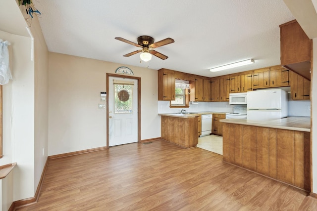 kitchen with white appliances, brown cabinetry, a peninsula, light countertops, and light wood-type flooring