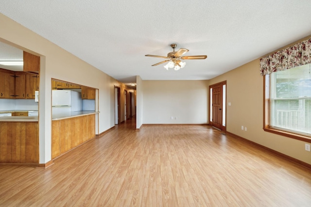 unfurnished living room with light wood-style floors, ceiling fan, a textured ceiling, and baseboards