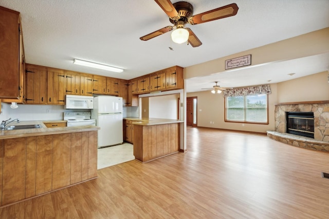 kitchen with white appliances, open floor plan, a peninsula, light countertops, and a sink