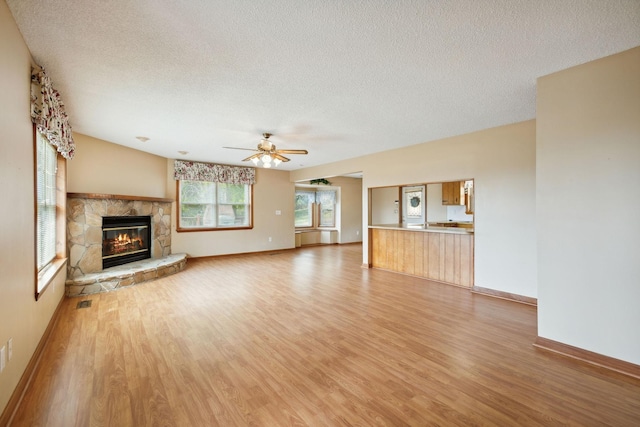 unfurnished living room with a textured ceiling, light wood finished floors, a fireplace, and a ceiling fan