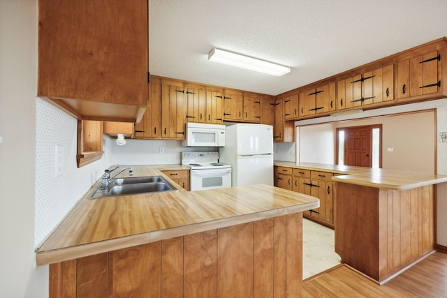 kitchen featuring a peninsula, white appliances, brown cabinets, and a sink