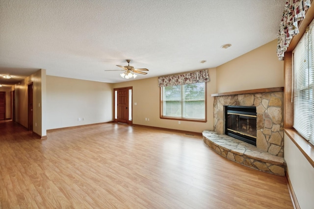 unfurnished living room with baseboards, a stone fireplace, a textured ceiling, and wood finished floors