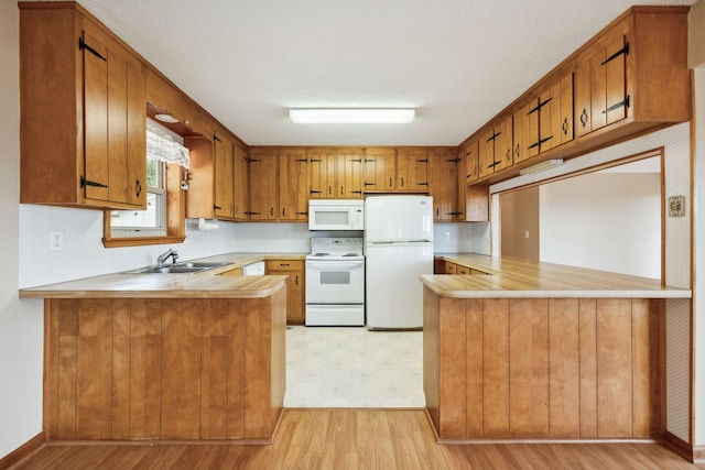 kitchen featuring brown cabinetry, white appliances, a sink, and a peninsula