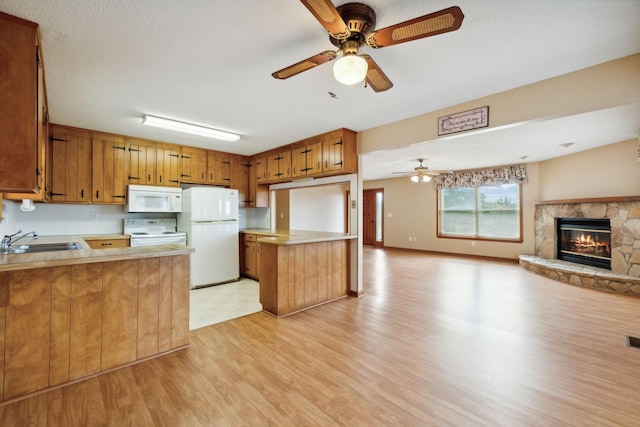 kitchen featuring white appliances, open floor plan, a peninsula, light countertops, and a sink