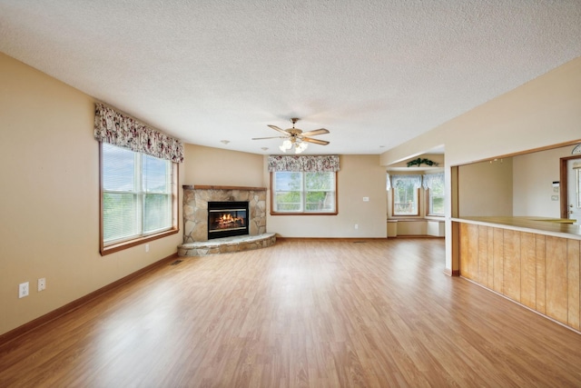 unfurnished living room featuring a healthy amount of sunlight, a fireplace, a textured ceiling, and light wood finished floors