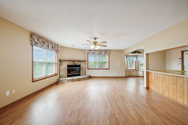 unfurnished living room with a wealth of natural light, light wood-type flooring, a stone fireplace, and a textured ceiling