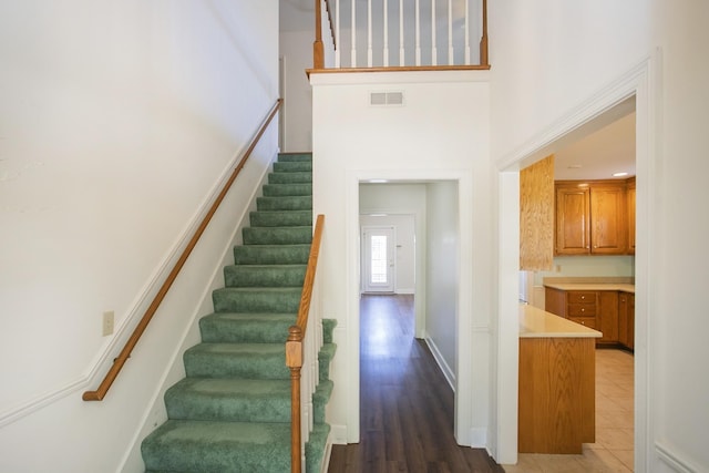 stairs featuring a towering ceiling, baseboards, visible vents, and wood finished floors