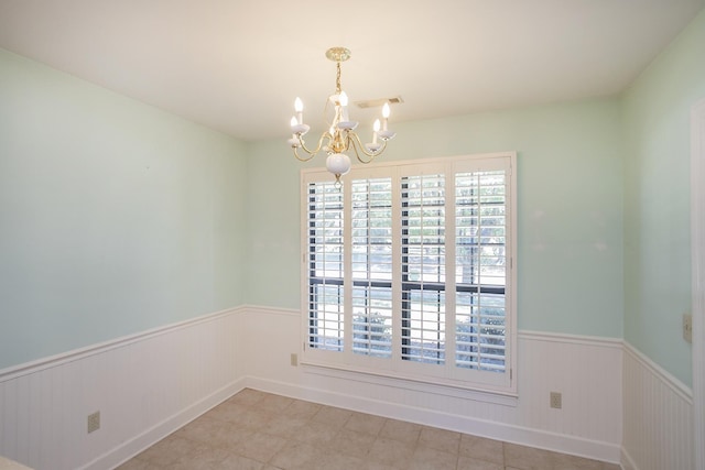 spare room featuring wainscoting, visible vents, and an inviting chandelier