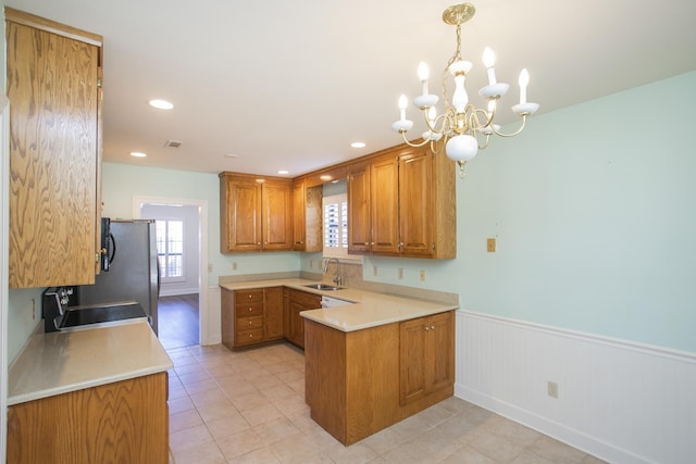 kitchen featuring brown cabinetry, a wainscoted wall, a peninsula, light countertops, and a sink