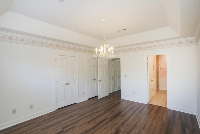 unfurnished bedroom with baseboards, dark wood-style flooring, a raised ceiling, and multiple closets