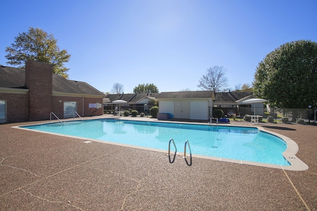 community pool with an outbuilding, a patio area, fence, and a shed