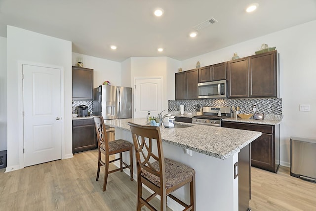 kitchen with visible vents, a breakfast bar area, stainless steel appliances, dark brown cabinets, and a sink