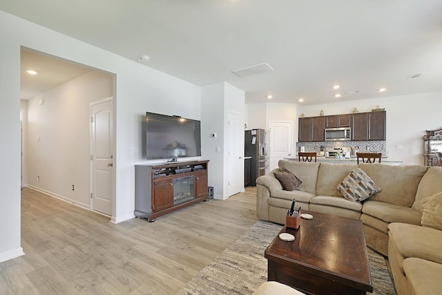 living room with light wood finished floors, baseboards, a glass covered fireplace, and recessed lighting