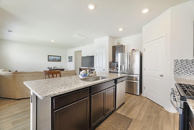 kitchen featuring tasteful backsplash, open floor plan, stainless steel appliances, light wood-type flooring, and a sink