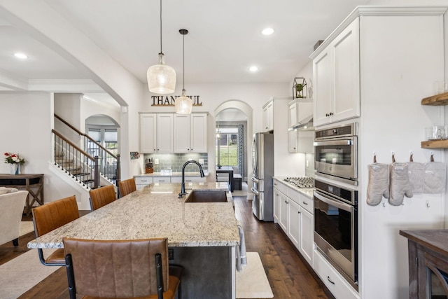 kitchen with arched walkways, stainless steel appliances, backsplash, and a sink