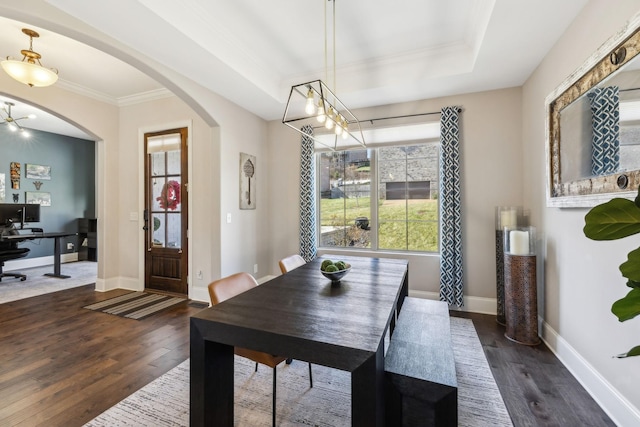 dining space with arched walkways, a raised ceiling, dark wood finished floors, and baseboards