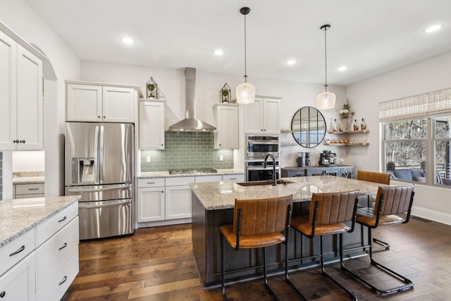 kitchen featuring dark wood finished floors, backsplash, appliances with stainless steel finishes, a sink, and wall chimney range hood