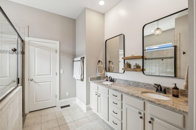 full bathroom with double vanity, tiled shower, tile patterned flooring, and a sink