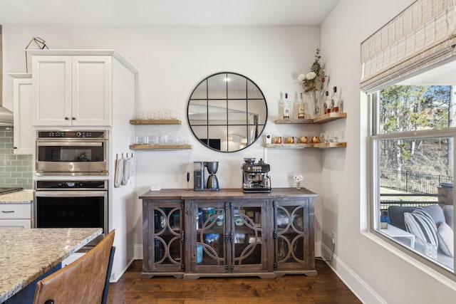 interior space with decorative backsplash, double oven, dark wood-type flooring, a bar, and baseboards