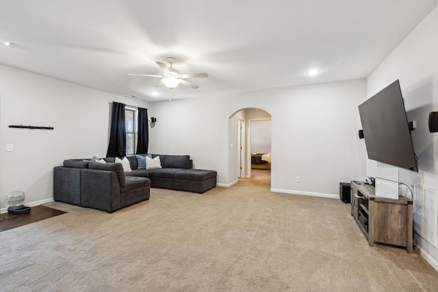 living area featuring arched walkways, ceiling fan, light carpet, and baseboards