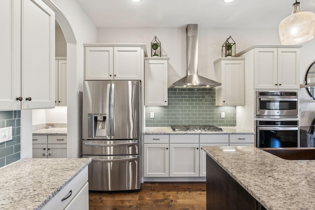 kitchen with dark wood-type flooring, wall chimney exhaust hood, stainless steel appliances, and backsplash