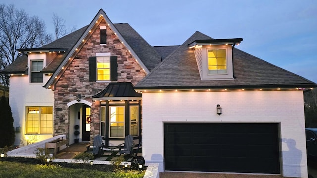 view of front facade with a shingled roof, metal roof, an attached garage, a standing seam roof, and brick siding