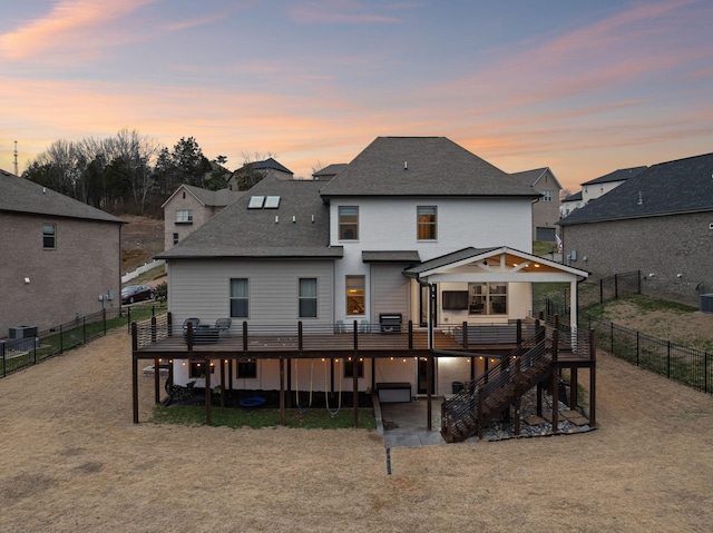 back of property at dusk featuring a fenced backyard, stairway, a shingled roof, and a wooden deck