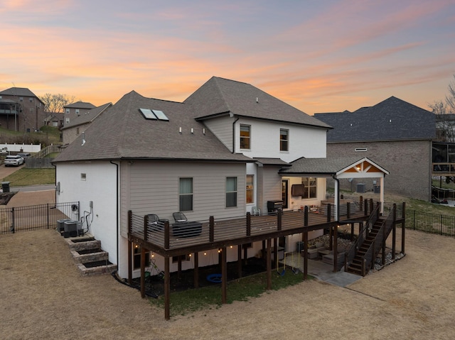 rear view of property with a wooden deck, stairway, a patio, fence, and a shingled roof