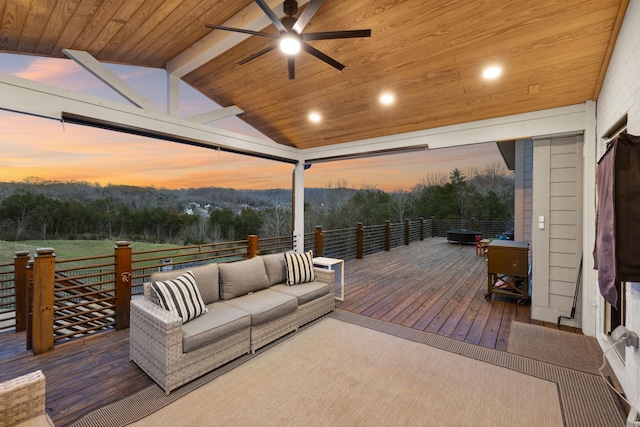 deck at dusk with a wooded view, outdoor lounge area, and a ceiling fan