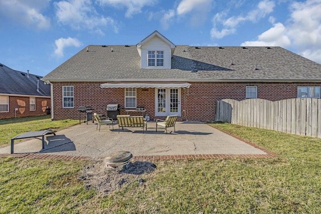 rear view of house featuring brick siding, a patio, a shingled roof, a lawn, and fence