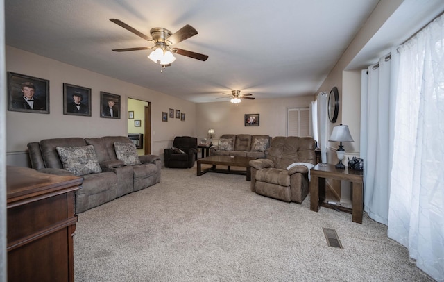 living area with visible vents, a ceiling fan, and light colored carpet