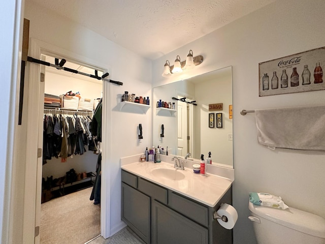 bathroom with a walk in closet, vanity, toilet, and a textured ceiling