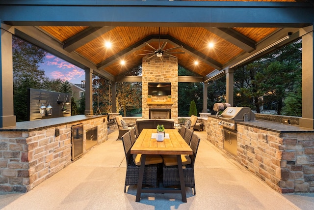 view of patio / terrace with an outdoor stone fireplace, grilling area, a gazebo, outdoor dining space, and exterior kitchen